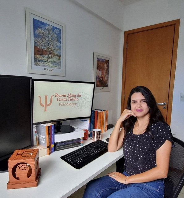 Psicóloga Bruna Fialho em seu consultório, ao lado de livros e computador.
